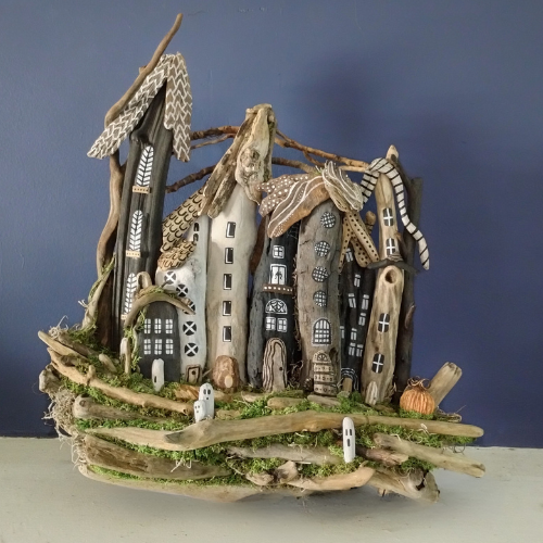 Halloween driftwood sculpture resembling a village with thatched roofs against a blue background