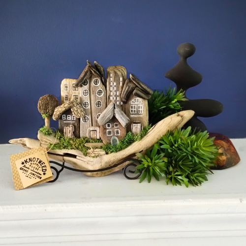 Decorative scene with driftwood miniature houses, trees, and a sign on a white surface with a blue background